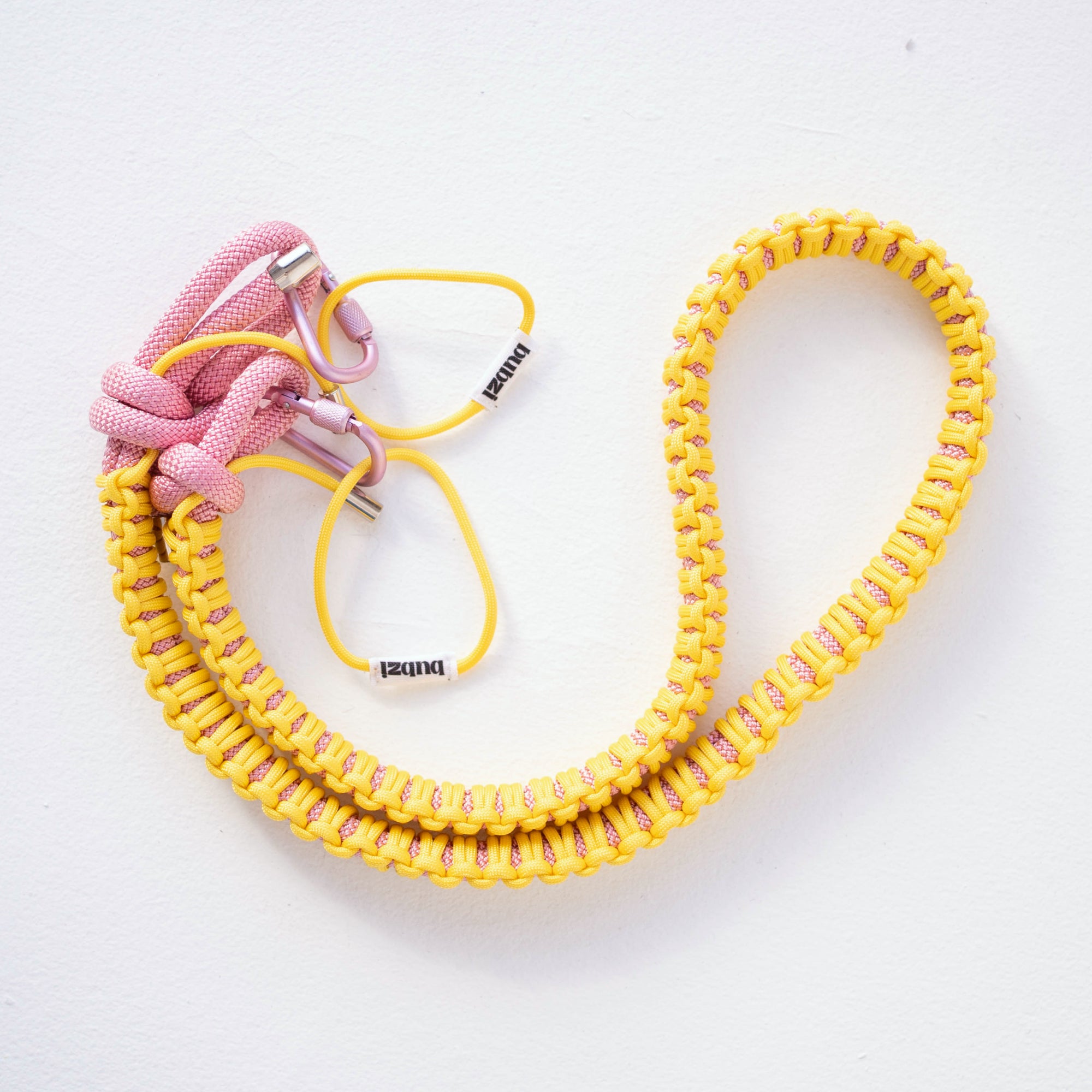 Yellow and pink Bubzi paracord camera strap on a white background