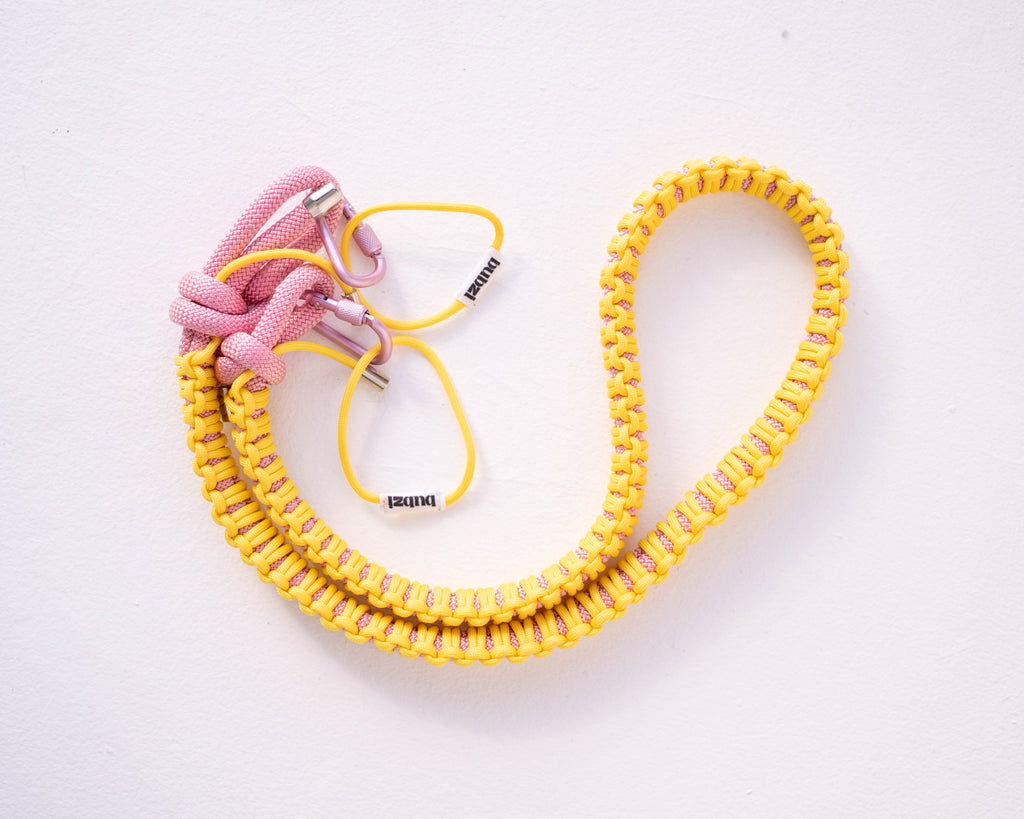 Yellow and pink Bubzi paracord camera strap with metal carabiners on a white background