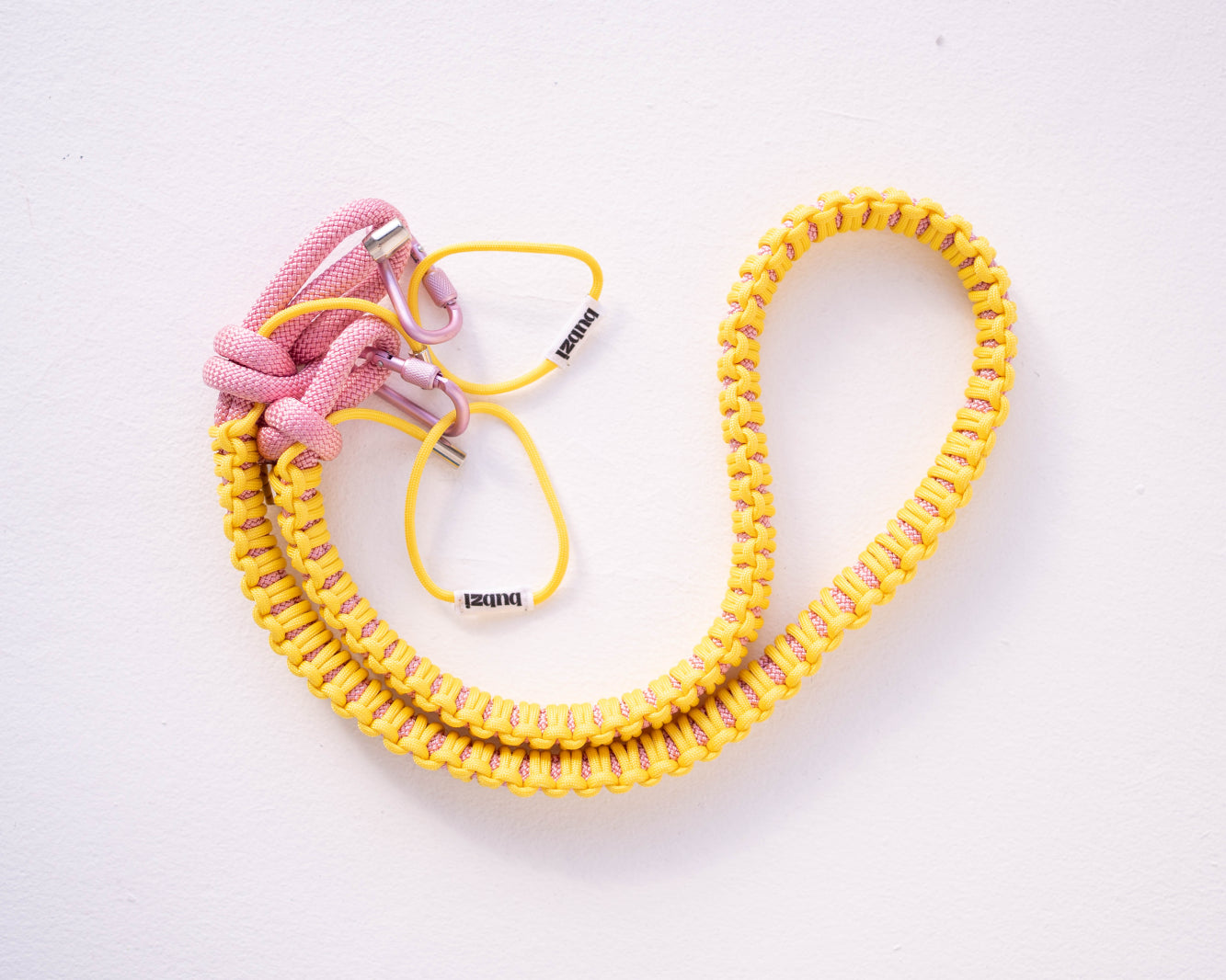 Yellow and pink Bubzi paracord camera strap with metal carabiners on a white background