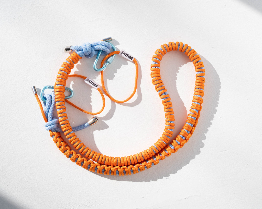 Orange and blue Bubzi paracord camera strap with metal carabiners on a white background