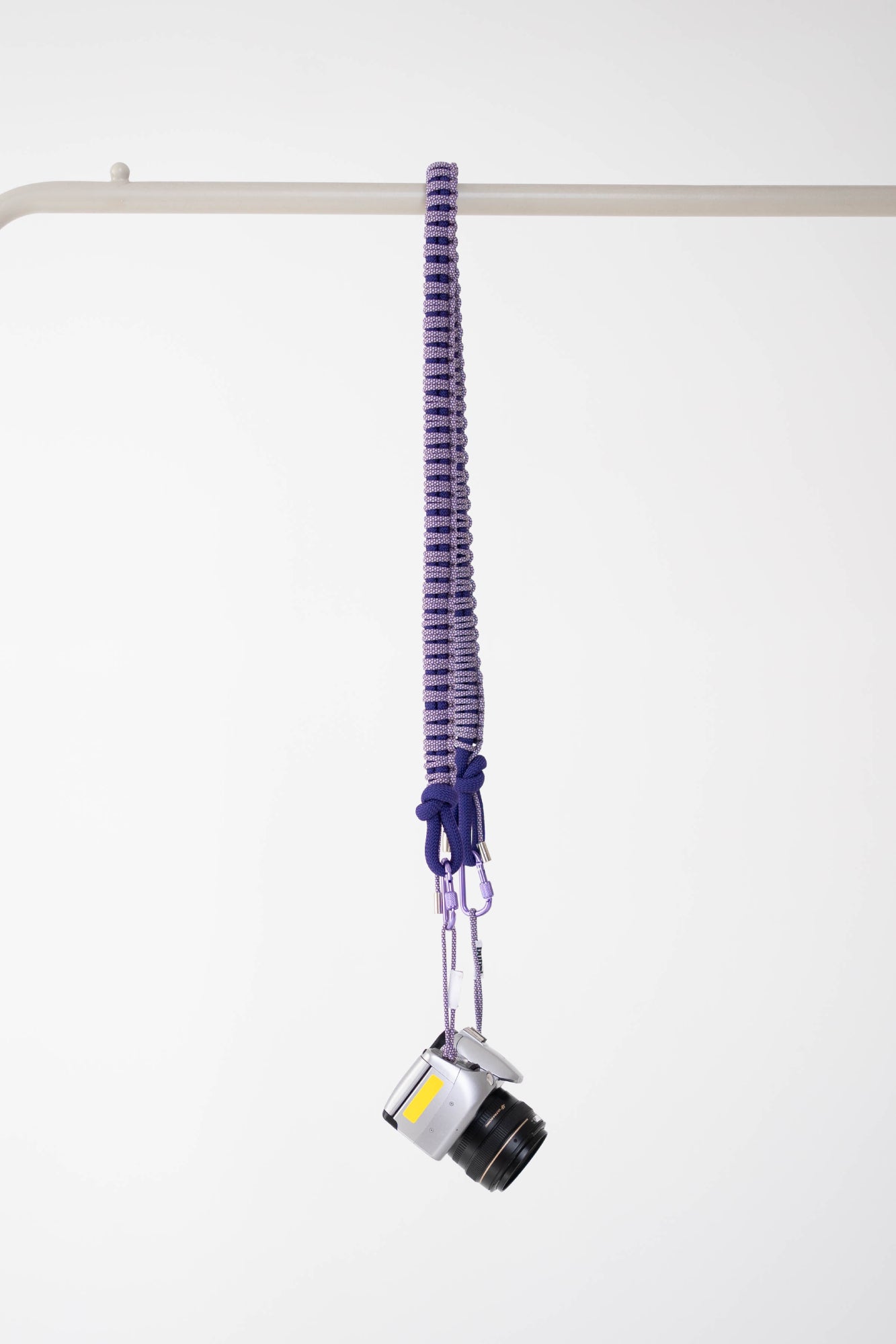 Purple snake print Bubzi camera strap hanging with a compact camera on a white studio background