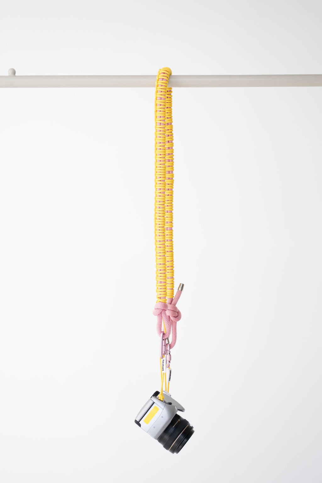 Yellow and pink Bubzi camera strap hanging with a compact camera on a white studio background