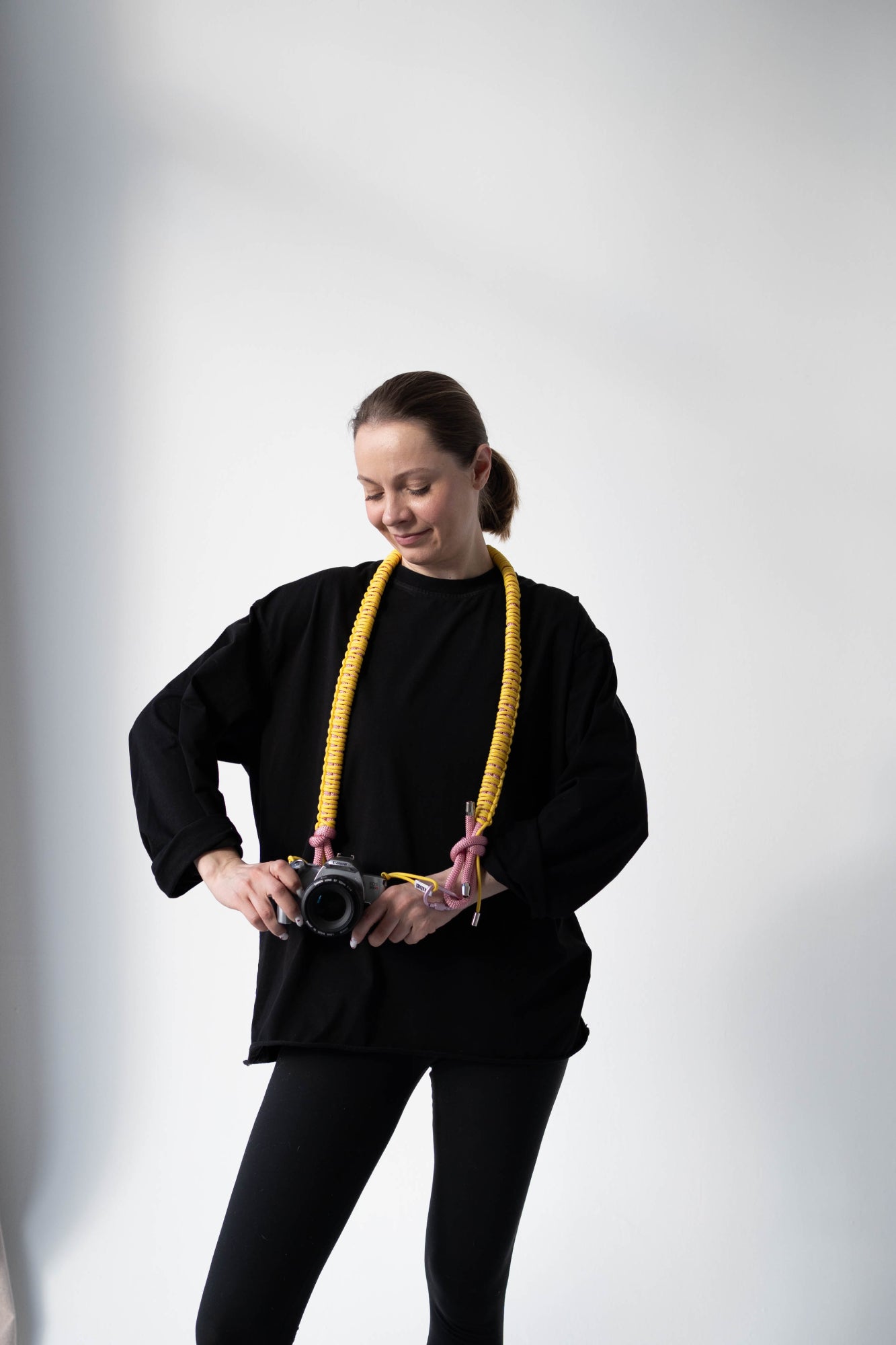 Model holding a camera with the yellow and pink Bubzi camera strap in a studio