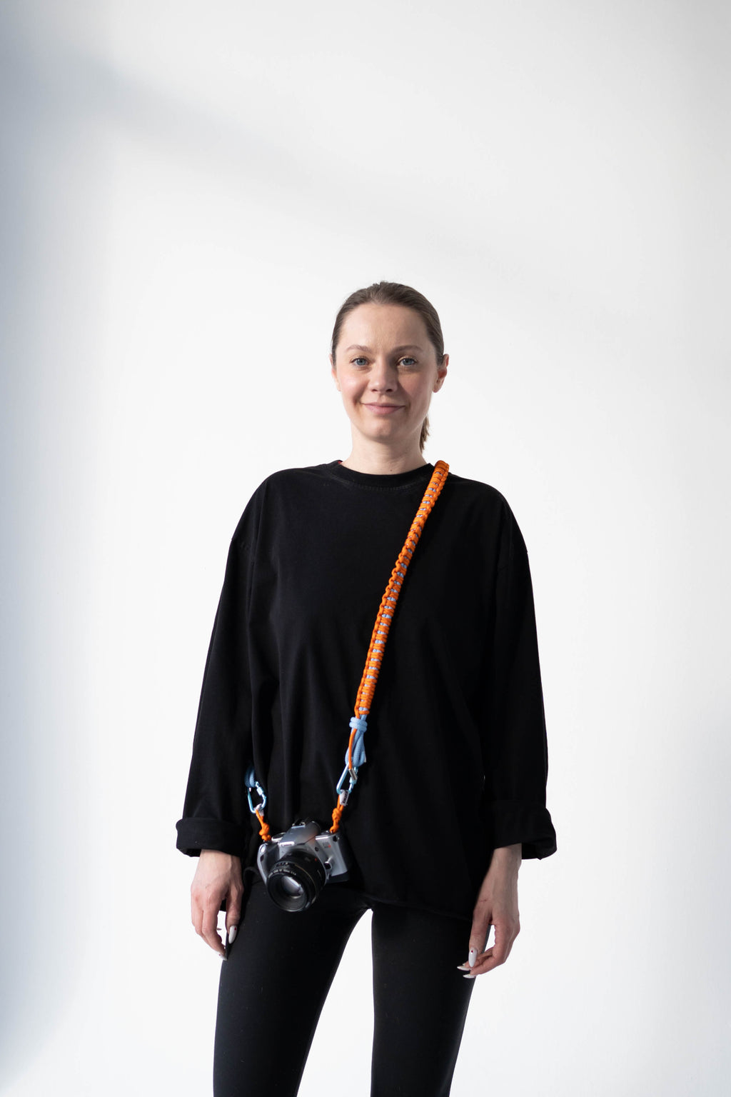 Front view of a model wearing the orange and blue Bubzi camera strap with a camera