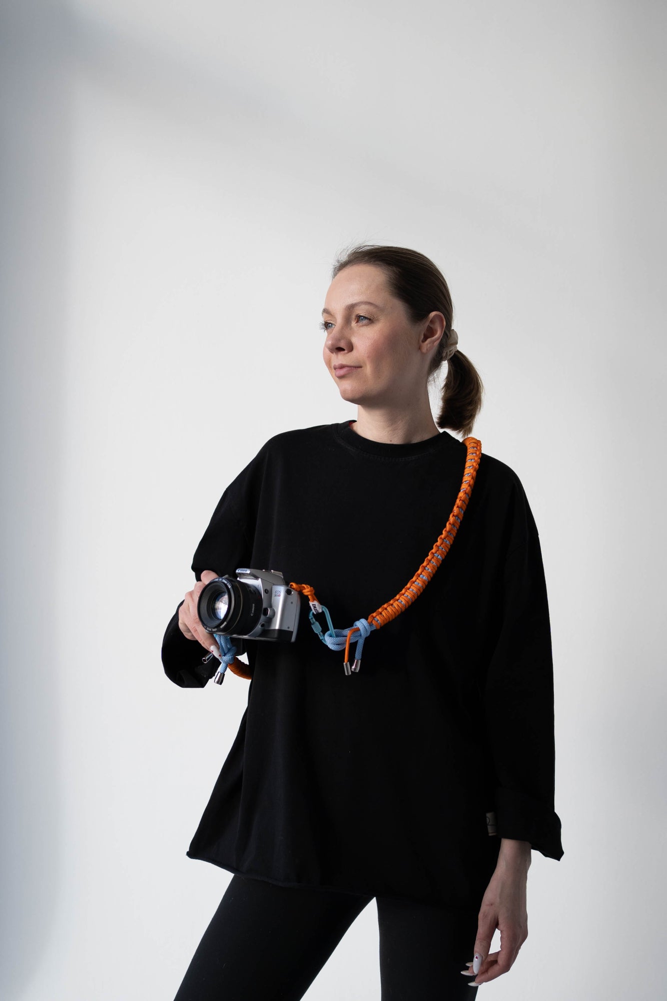 Model wearing an orange and blue Bubzi camera strap attached to a compact camera