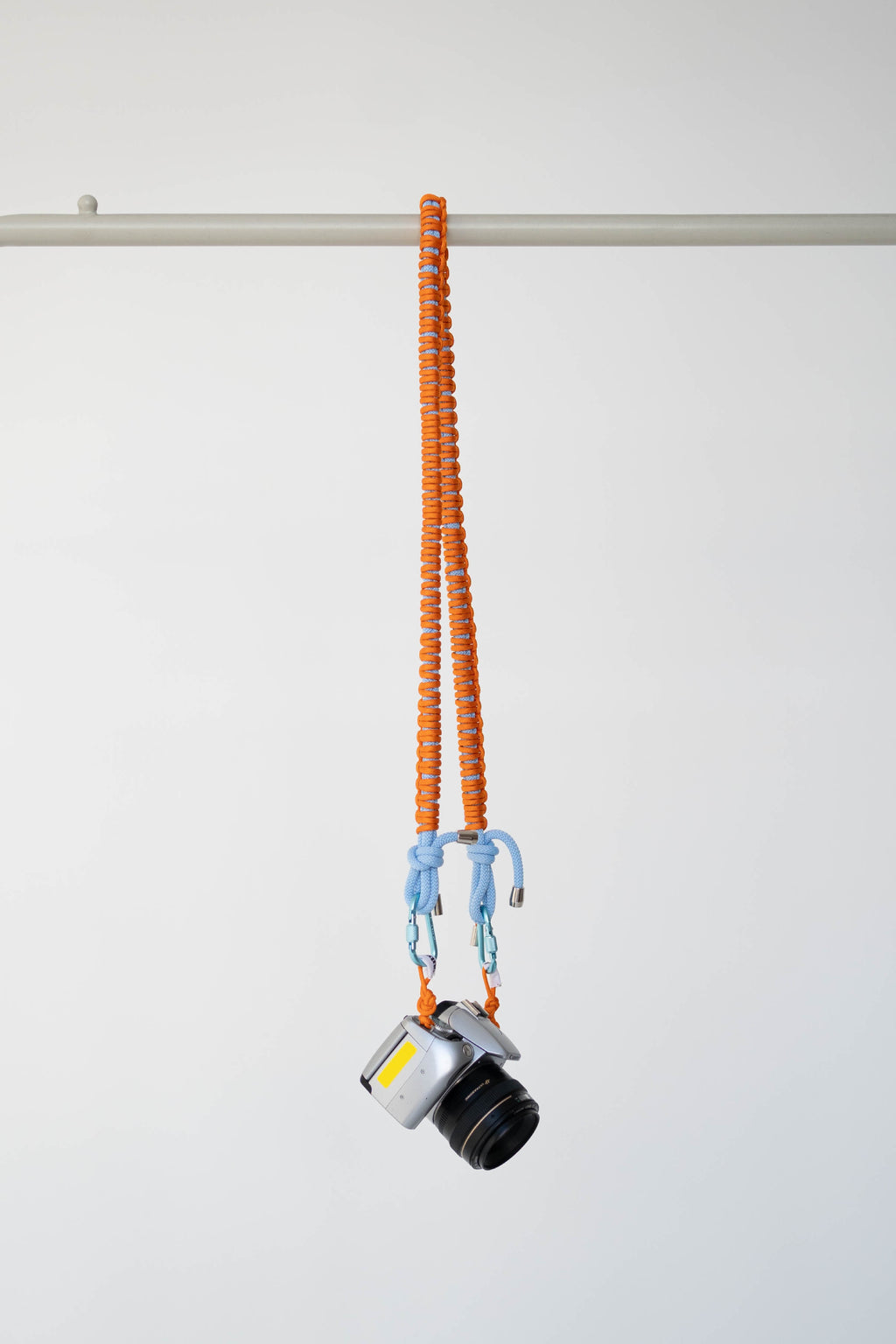 Orange and blue Bubzi camera strap hanging with a camera on a white studio background