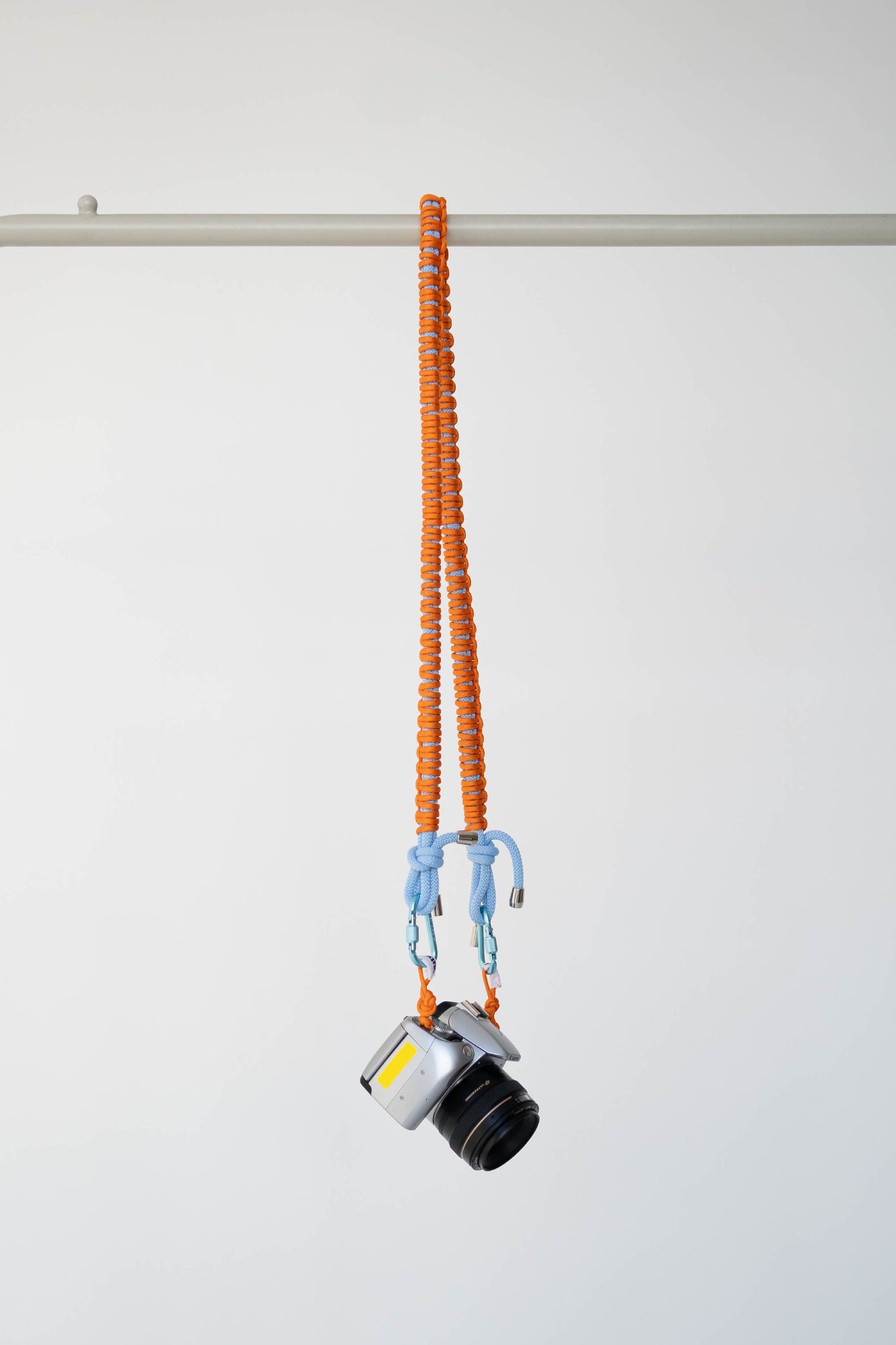 Orange and blue Bubzi camera strap hanging with a camera on a white studio background