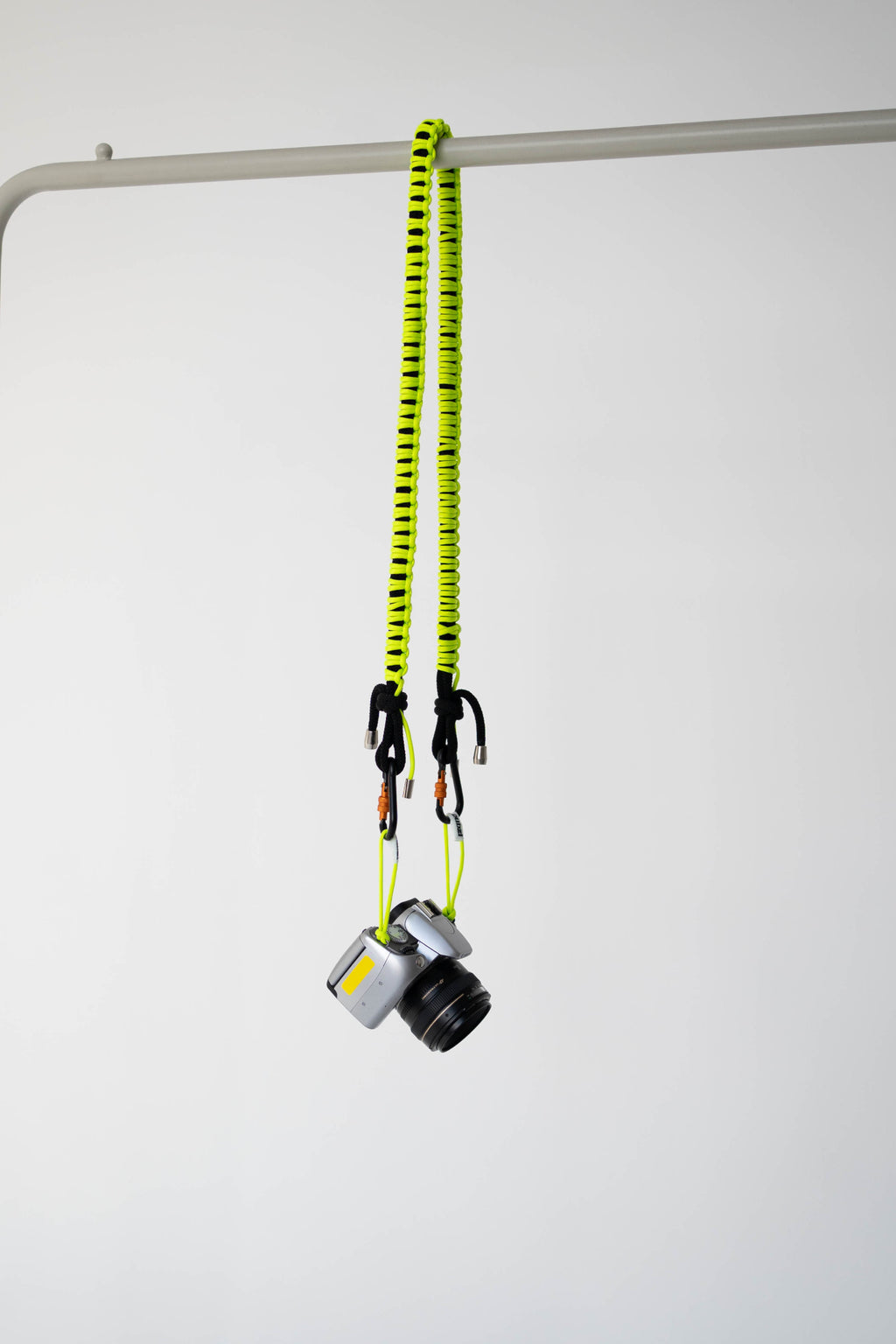 Black and lime Bubzi camera strap hanging with a compact camera on a white studio background