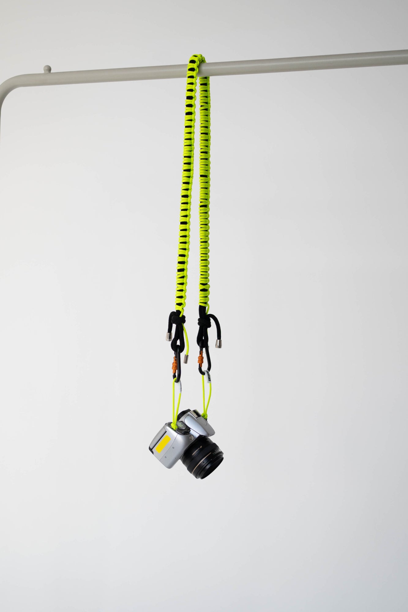Black and lime Bubzi camera strap hanging with a compact camera on a white studio background