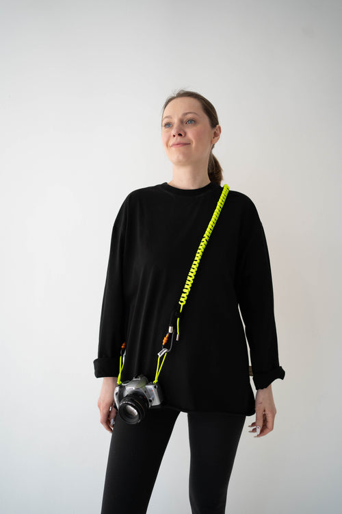 Model wearing a black and lime Bubzi camera strap attached to a compact camera