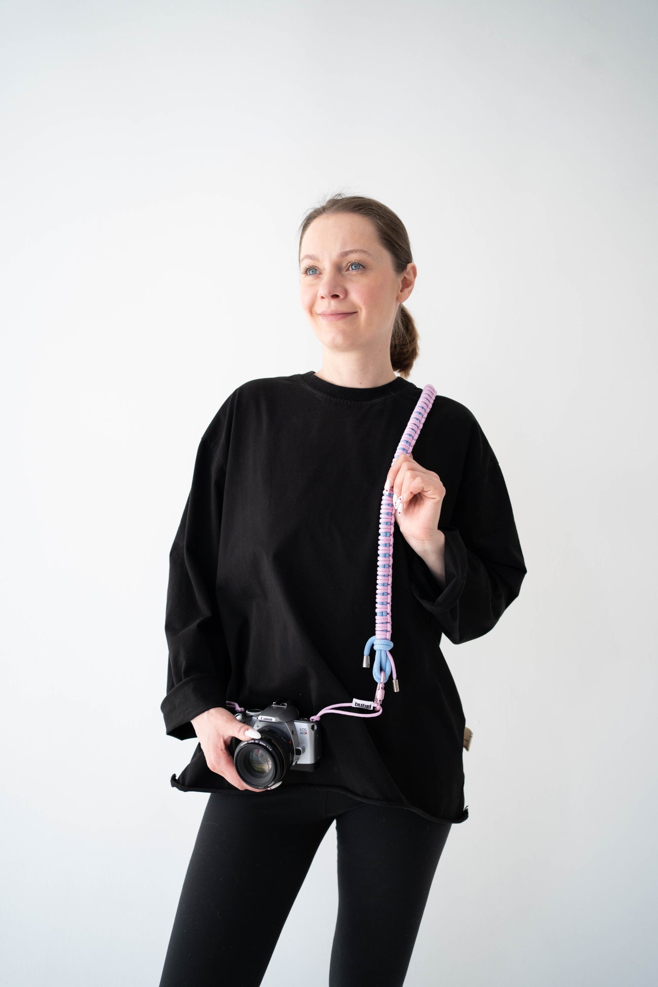 Model holding a camera with the pink and blue Bubzi paracord strap in a studio