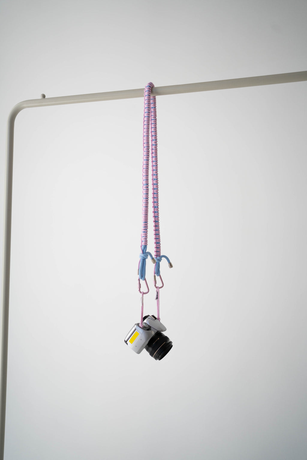 Pink and blue Bubzi camera strap hanging with a compact camera on a white studio background