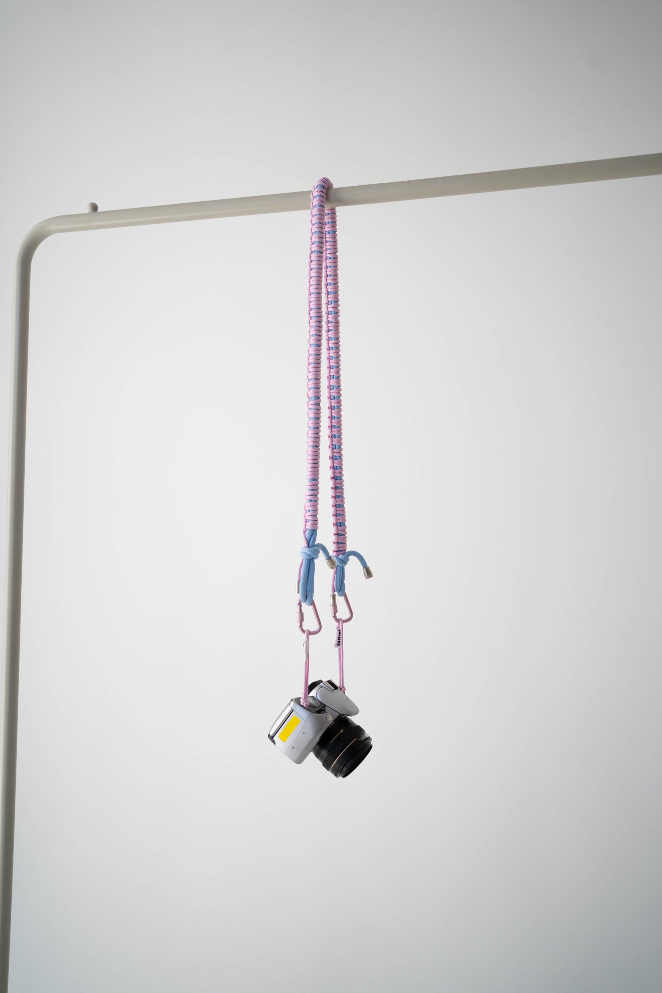 Pink and blue Bubzi camera strap hanging with a compact camera on a white studio background