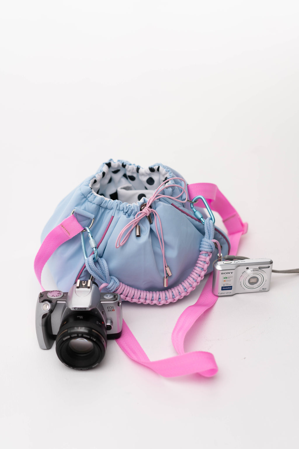 Blue Mini Bubzi camera bag placed next to a Canon camera and compact Sony camera
