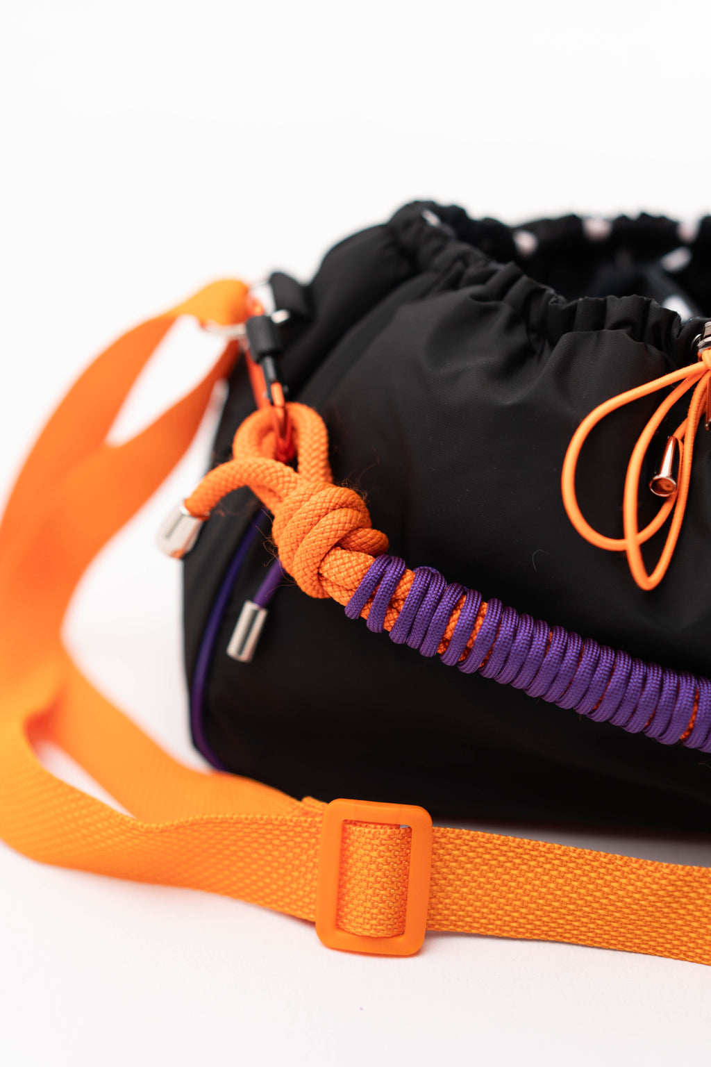 Front view of the black Mini Bubzi bag with orange strap, purple handle, and soft gathered opening