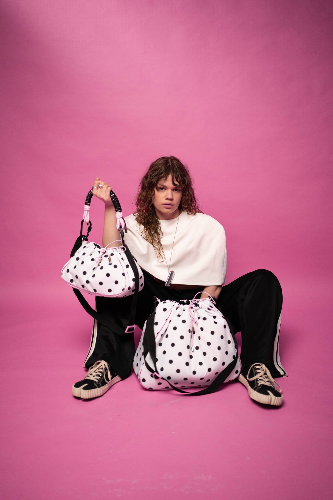 Model sitting with Mini and Maxi Bubzi polka dot bags on a pink studio background