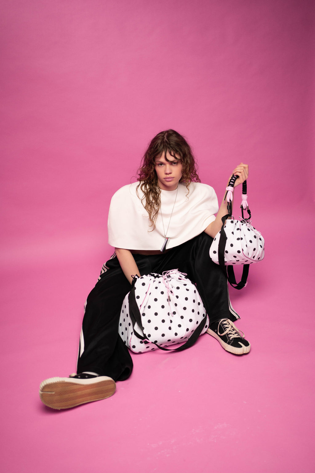 The model is sitting with polka dot Maxi Bubzi bags against a pink studio background.