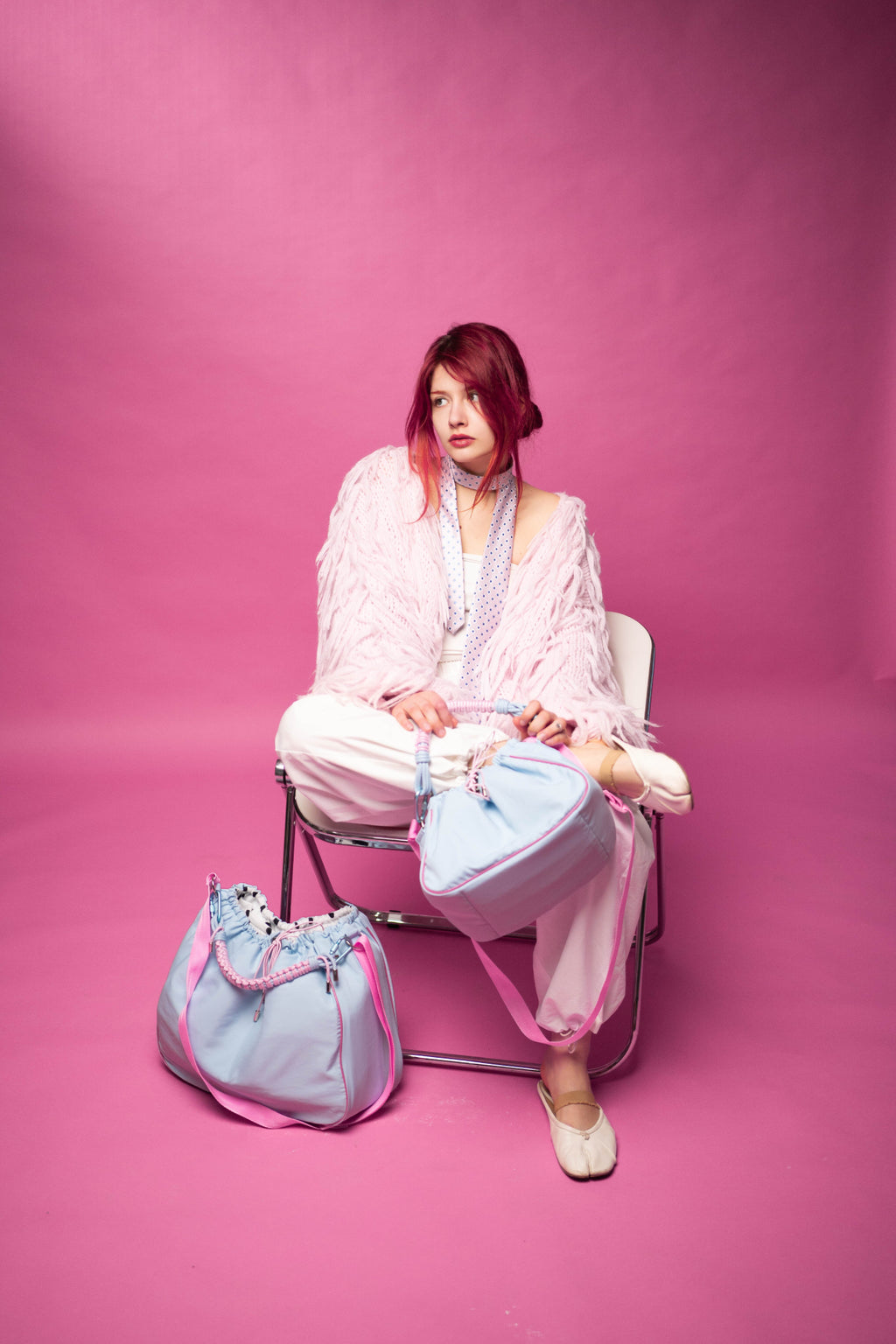 The model is sitting with a light blue Maxi Bubzi camera bag against a pink studio background.