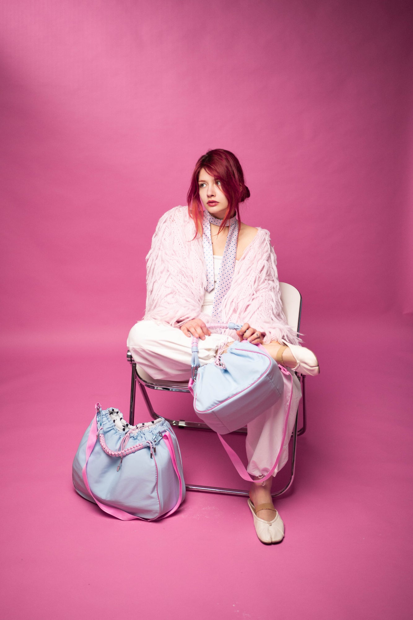 The model is sitting with a light blue Maxi Bubzi camera bag against a pink studio background.