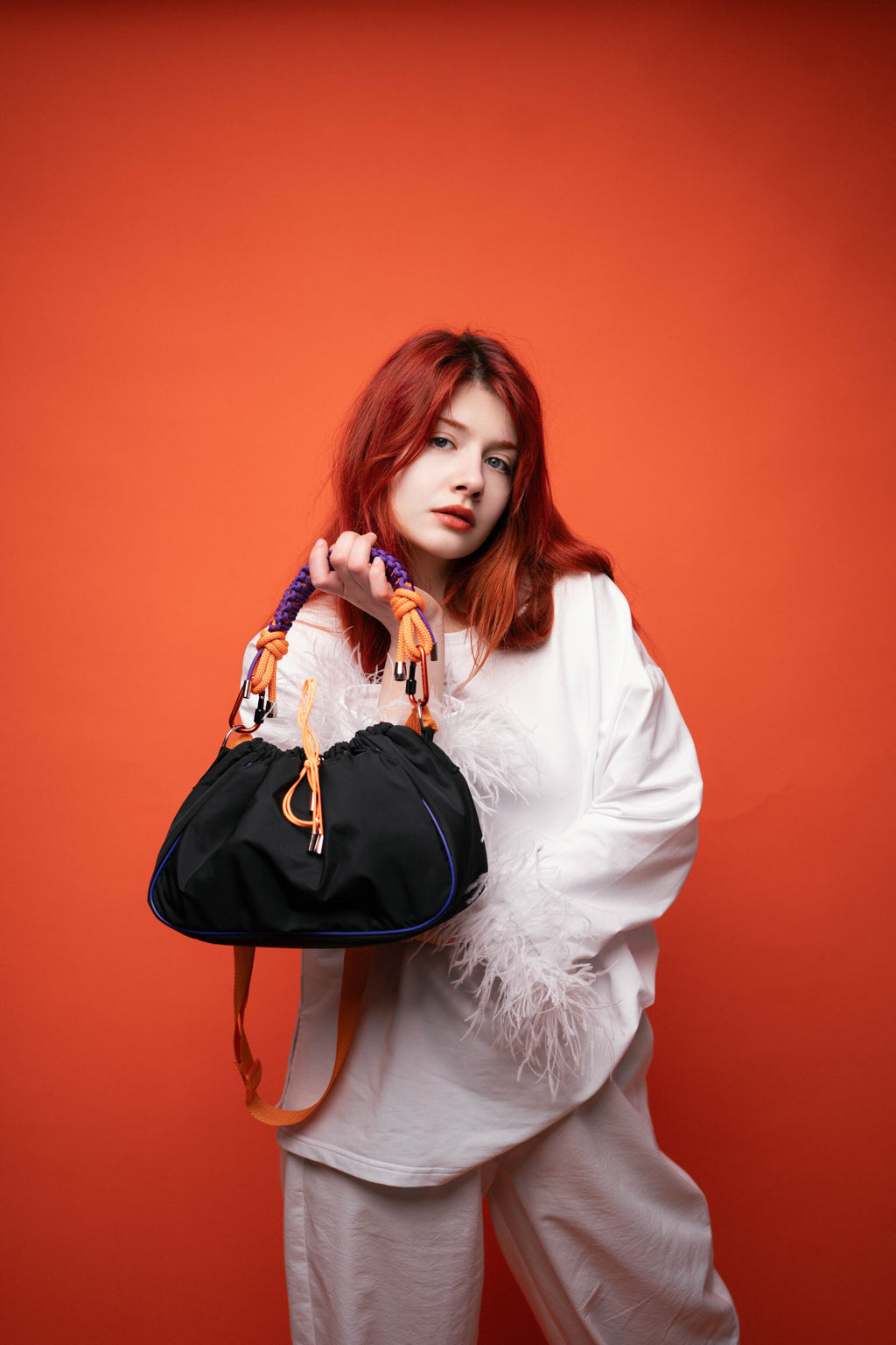 Model sitting with a black Mini Bubzi bag and orange shoulder strap on a light studio background
