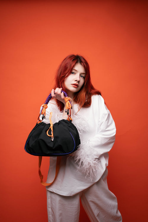 Model sitting with a black Mini Bubzi bag and orange shoulder strap on a light studio background